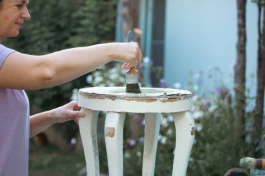 Orta yaşlı bir kadın ahşap mobilya boyuyor. Yepyeni renkli tebeşir boyasıyla eski moda ahşap mobilyaları yeniliyorum. Ev dekorasyonu yeniden biçimlendiriliyor