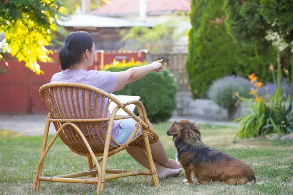 Sıradan, orta yaşlı bir kadın bahçede küçük kahverengi köpeğiyle eğleniyor. Hayvanlarla bağ kurma ve birlikte olmaktan keyif alma kavramı.