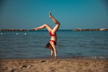 Mutlu kız sahilde amuda kalkıyor. Seyahat, yaz, tatil, enerji kavramı.