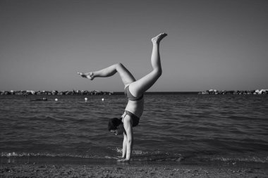 Mutlu kız sahilde amuda kalkıyor. Seyahat, yaz, tatil, enerji kavramı.