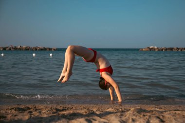 Mutlu kız sahilde amuda kalkıyor. Seyahat, yaz, tatil, enerji kavramı.
