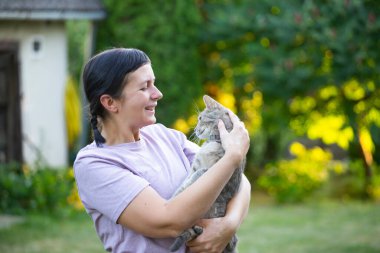 Orta yaşlı bir kadın sevimli kedisini dışarıda tutuyor..