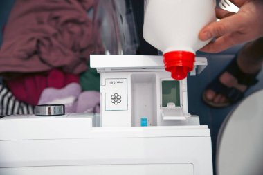 Çamaşır yıkamadan önce çamaşır makinesine çamaşır deterjanı döken bir erkek.