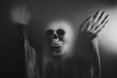Creepy skeleton figure with skull behind matte glass. Halloween festival concept.Blurred picture