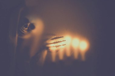 Creepy skeleton figure with skull and candle lights behind matte glass. Halloween festival concept.Blurred picture
