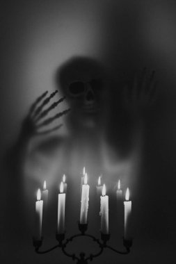 Creepy skeleton figure with skull and candlelights behind matte glass. Halloween festival concept.Blurred picture