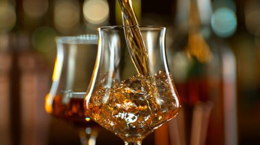 Close-up of pouring whiskey or rum on the bar, dark toned background