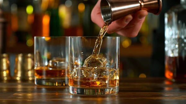 Close-up of pouring whiskey or rum on the bar, dark toned background