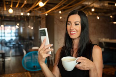 İş kadını, iş yerinde akıllı telefonuyla selfie çekiyor. Modern ofiste çalışan kendine güvenen kadın muhasebeci.