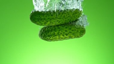 Yeşil eğimli arka planda suya düşen taze salatalıkların süper yavaş çekimi. Yüksek hızlı sinema kamerası, 1000 fps..