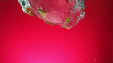 Kırmızı gradyan arkaplanda taze pitahaya 'nın suya düşmesi süper yavaş bir hareket. Yüksek hızlı sinema kamerası, 1000 fps..