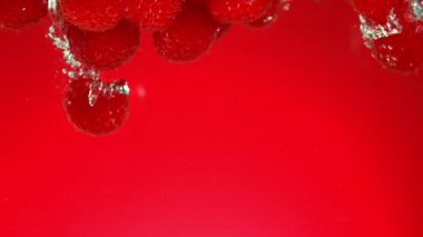 Kırmızı gradyan arkaplanda suya düşen taze ahududu süper yavaş çekimde. Yüksek hızlı sinema kamerası, 1000 fps..