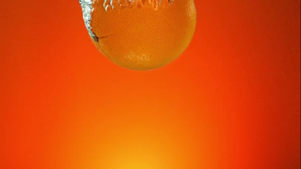 Сверхмедленное Движение Падения Свежего Апельсина Воду Оранжевом Фоне Снято Камеру — стоковое видео
