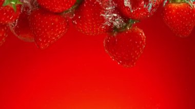 Kırmızı gradyan arkaplanda suya düşen taze çileklerin süper yavaş çekimleri. Yüksek hızlı sinema kamerası, 1000 fps..