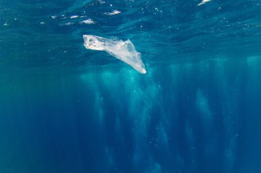 Mavi derinlikte suyun altında yüzen plastik torba, çevresel kirlilik. Okyanusun plastik kirliliği