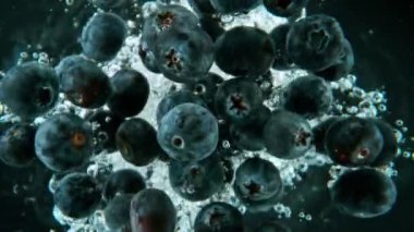 Düşen yaban mersinlerinin suya düşüşünün süper yavaş çekimi, siyah arka plan, sualtı bakış açısı. 1000 fps hızla yüksek hızlı sinematik kamera ile çekildi..