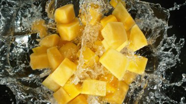 Fresh mango pieces falling into water, top down view