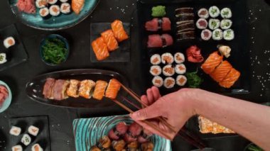 Geleneksel Japon mutfağının en iyi manzarası. Somon, ton balığı ve sebzeli suşi ruloları siyah taş masada servis edilir. Siyah taş üzerinde yemek çubuklarıyla Asya yemeği. Kamera hareketi .
