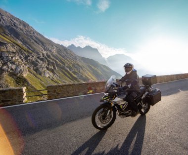 Gün doğumunda İtalyan Alplerinde motosikletli gezgin, dramatik bir gökyüzü. Seyahat ve özgürlük, açık hava aktiviteleri