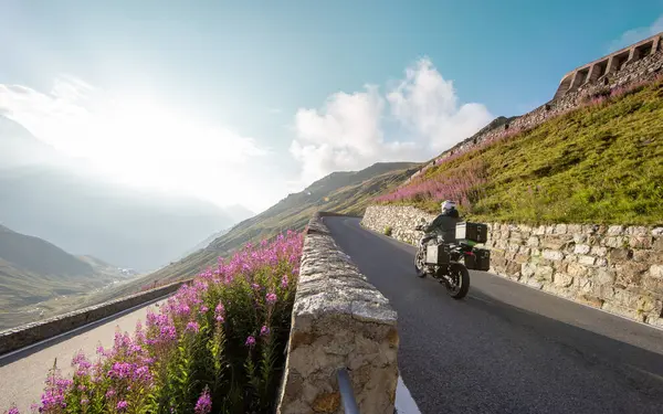 stock image Motorbiker riding in Italian Alps during sunrise, dramatic sky. Travel and freedom, outdoor activities