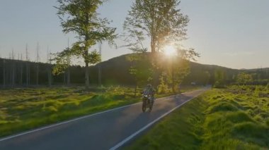 Boş asfalt yolda motosiklet süren sürücü, gün batımında bahar dağları