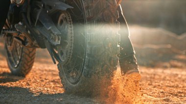 Yarışın başlangıcında motosikletin tekerinden uçan kayalar ve toz.