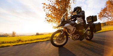 Günbatımında, sonbahar dağlarında, boş yolda motosiklet sürmek