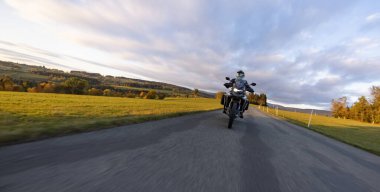 Günbatımında, sonbahar dağlarında, boş yolda motosiklet sürmek