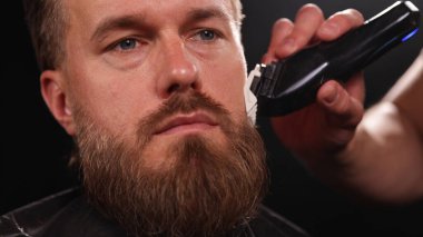 Berber dükkanındaki sakallı genç adam. Berber saç kesimini hazırlıyor. Karanlık Atmosfer, Kara Arkaplan. Berber ve Müşteri kavramı.