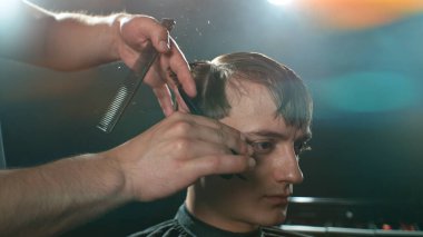 Berber dükkanındaki sakallı genç adam. Berber saç kesimini hazırlıyor. Karanlık Atmosfer, Kara Arkaplan. Berber ve Müşteri kavramı.