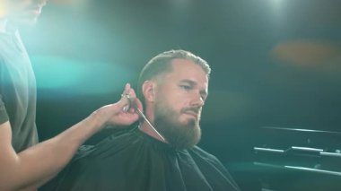 Berber dükkanındaki sakallı genç adam. Berber saç kesimini hazırlıyor. Karanlık Atmosfer, Kara Arkaplan. Berber ve Müşteri kavramı.