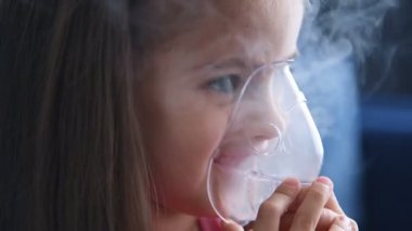 Küçük mutlu kız nebulizörle nefes alıyor. Çocuk astımlı nebulizör buharlı öksürük konsepti. Kapat.