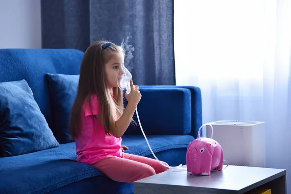 stock image Little girl with inhaler on sofa at home in the living room. Health care and medical concept.