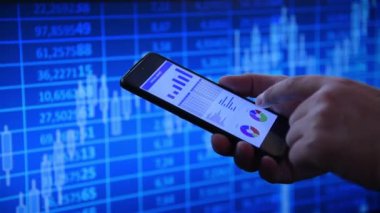 Finansal tabloları gösteren akıllı bir telefon kullanarak canlı bir mavi borsa geçmişine karşı bir elin yakın çekimi. Ticaret kavramı