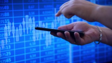 Akıllı telefon kullanarak canlı bir mavi borsa geçmişine karşı. Ticaret kavramı. Yavaş Hareket Efekti.
