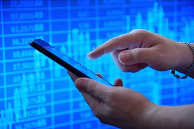 Finansal tabloları gösteren akıllı bir telefon kullanarak canlı bir mavi borsa geçmişine karşı. Ticaret kavramı