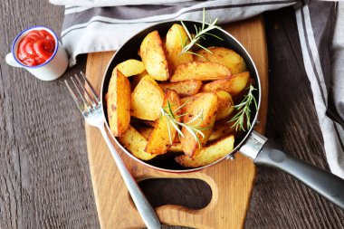 Ahşap arka planda, dökme demir tavada taze biberiyeli kızarmış patates. Üst görünüm.