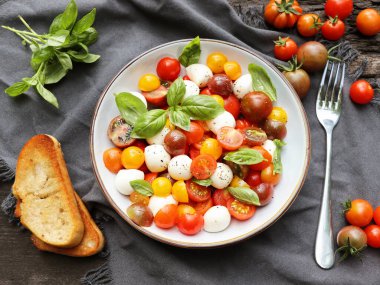 Domatesli Caprese Salatası, fesleğen, mozarella, zeytinyağı ve ahşap zemin üzerinde zeytin yağı. İtalyan geleneksel Caprese salata malzemeleri. Akdeniz, organik ve doğal gıda konsepti.