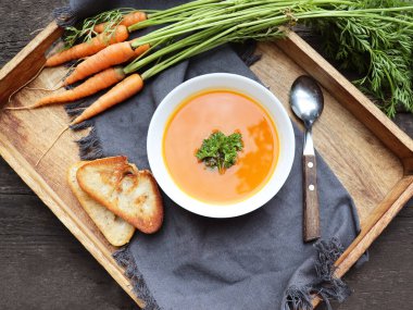 Tahta zemin üzerinde taze havuç bulunan bir kase havuç çorbası. Kahverengi masada maydanozlu havuç çorbası. Bahar sebze çorbası. Ev yapımı krema çorbası.