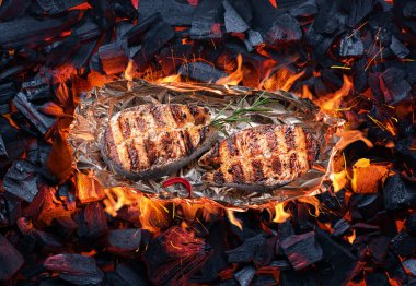 Kavrulmuş somon bifteği alüminyum folyoyla sıcak kömür parçalarının üzerinde barbekü ızgarası. Üst görünüm.