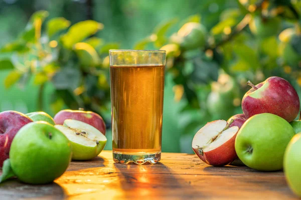 新鲜的苹果汁和有机苹果放在木制桌子上 夕阳西下的夏园 — 图库照片