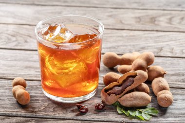 Glass of cool refreshing tamarind drink and some tamarind fruit on wooden table.