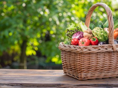 Hasır sepetteki taze organik sebzeler ve bitkiler. Arkaplanda bulanık yeşil doğa. 