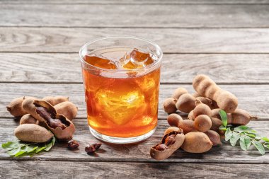 Bir bardak ferahlatıcı demirhindi içeceği ve ahşap masada biraz demirhindi meyvesi..