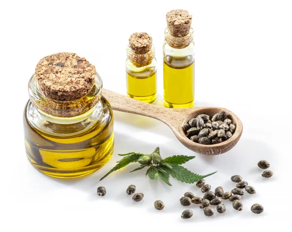 Ahşap kaşıkta esrar tohumları ve beyaz arka planda izole edilmiş kenevir yağı şişeleri. Kapat..