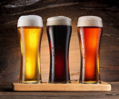 Three chilled glasses of different beer on wooden table closeup. 
