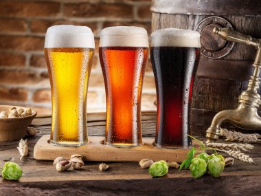 Three chilled glasses of different beer and beer barrel on wooden table closeup. 