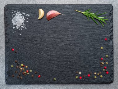 Natural stone black slate serving plate with seasonings and spices arranged as a frame. Flat lay. clipart