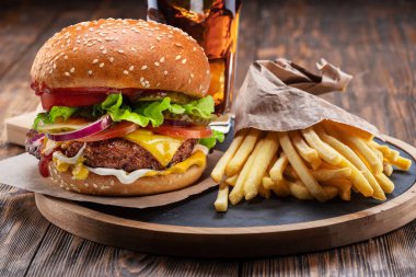 Tasty cheeseburger or hamburger, glass of cola and french fries on wooden tray close-up.