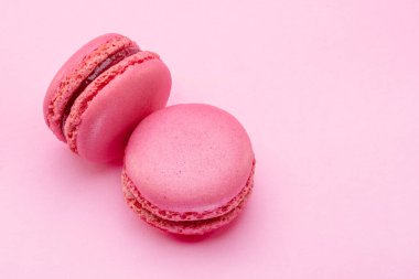 Two pink french macarons isolated on pink background.